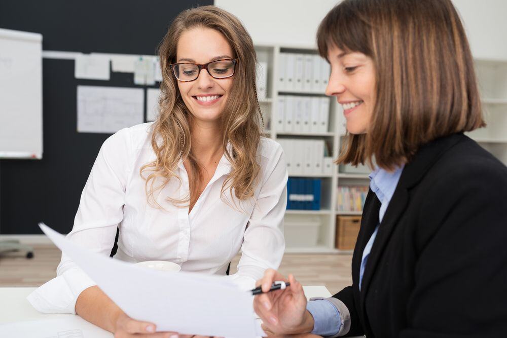 Close up Two Happy Young Businesswomen at the Office Talking About Business Report on Paper. Close up Two Happy Young Businesswomen at the Office Talking About Business Report on Paper.